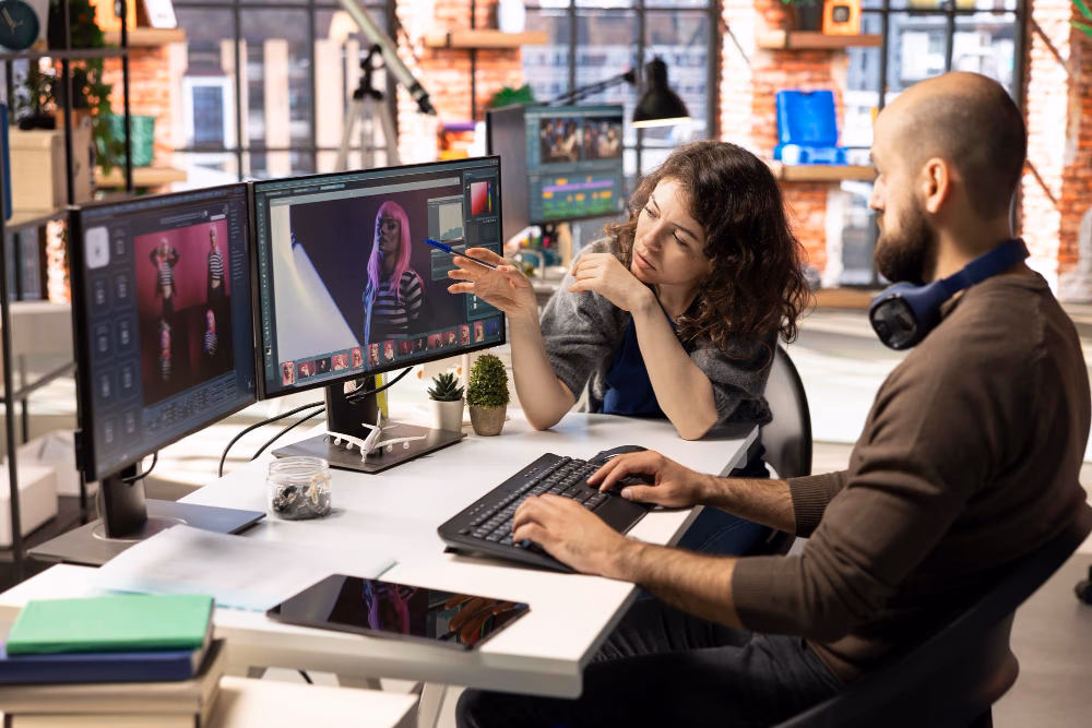Two creatives working together at monitors in a bright office